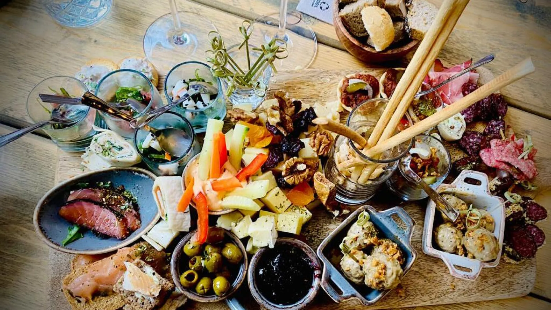 Schmankerlplatte mit Fleisch, Käse, Gemüse und Dips auf einem Holzbrett.